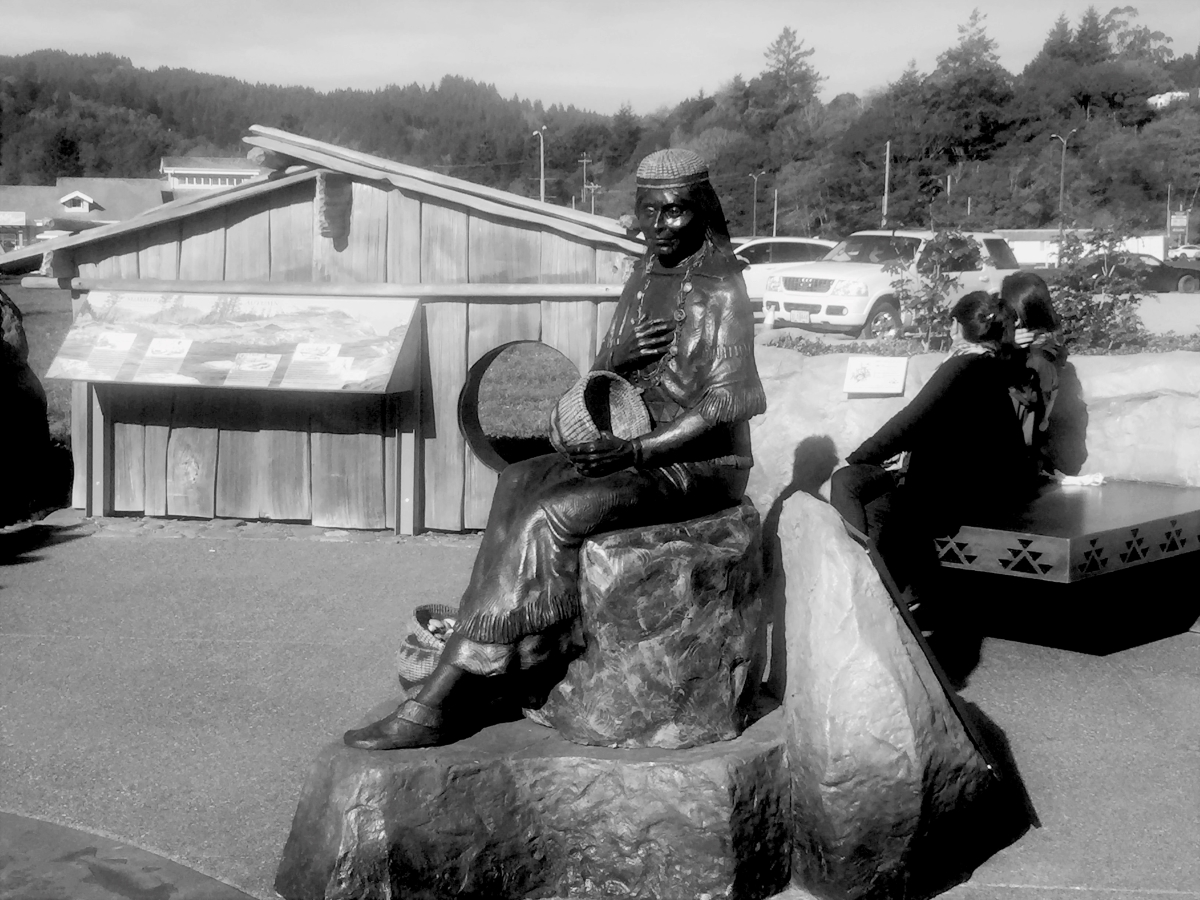 Statue in a park with people sitting on a bench